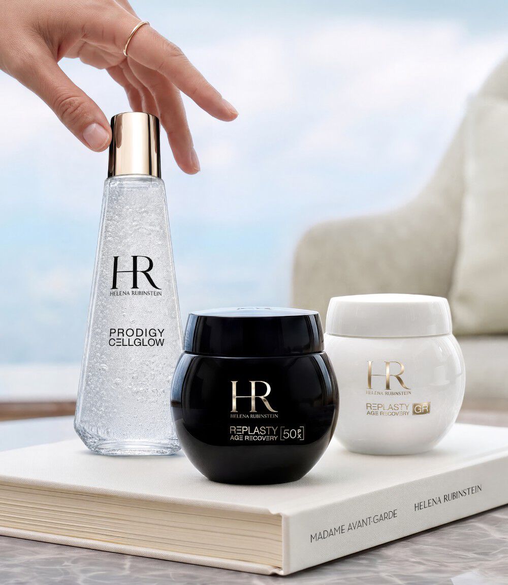 Trois produits de soin Helena Rubinstein (Prodigy Cellglow et Re-Plasty) disposes sur un livre blanc devant une fenetre avec vue sur un paysage.​