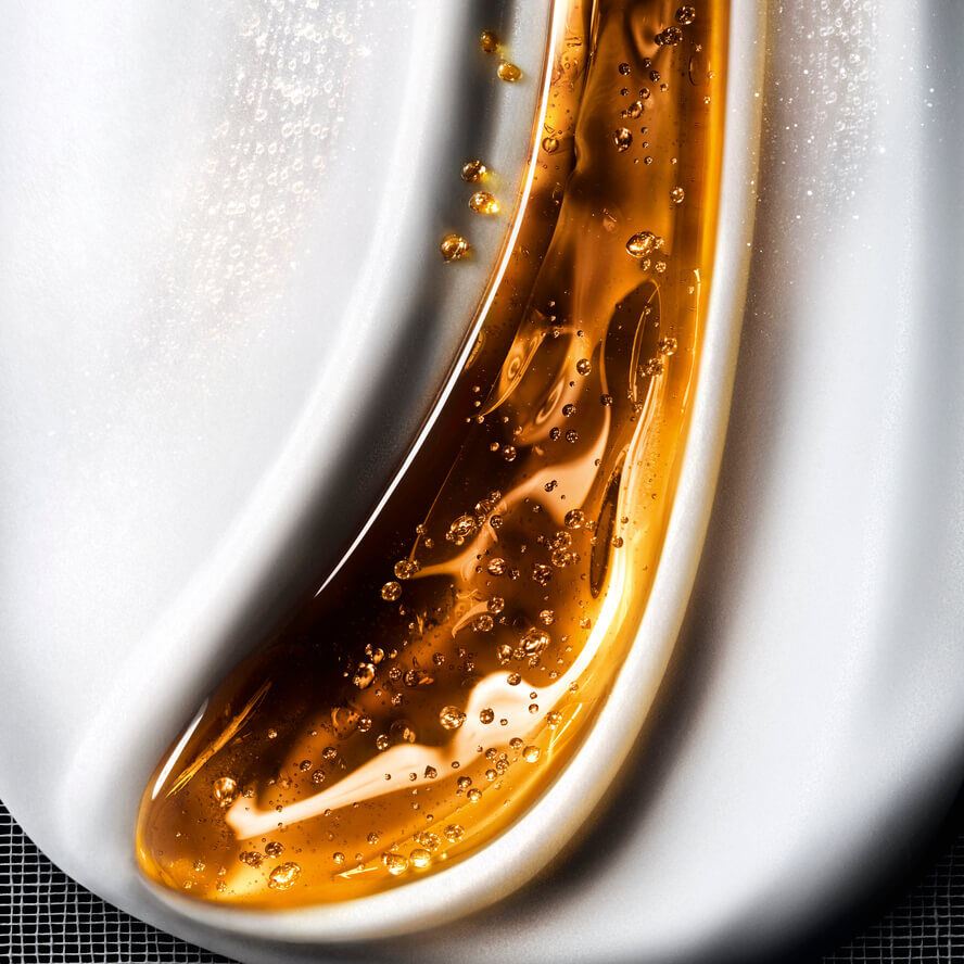 Gros plan d'une texture cosmetique fluide, melangeant des vagues de gel dore brillant avec des bulles sur un fond blanc cremeux, evoquant un soin riche.