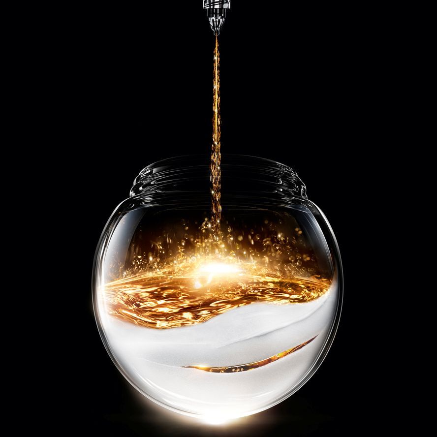 Un liquide dore petillant se verse dans un pot en verre spherique, reposant sur une base blanche texturee, creant un contraste lumineux sur fond noir.