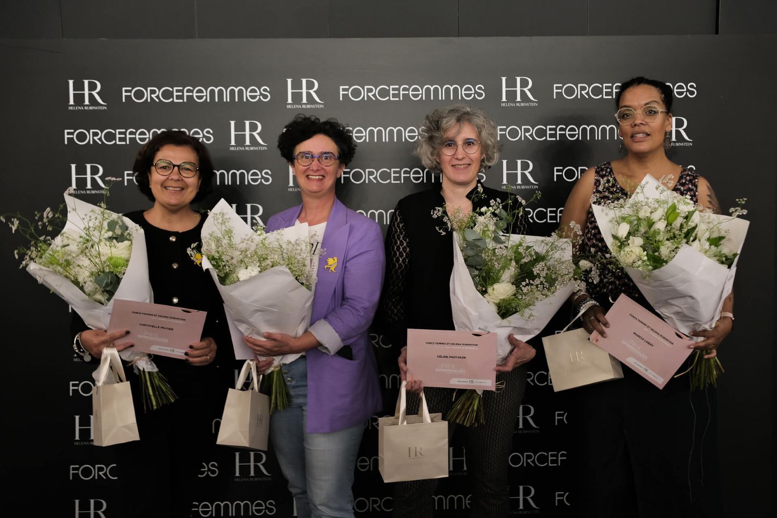 Quatre femmes souriantes recoivent des bouquets de fleurs blanches et des certificats, posant devant un mur noir avec les logos "HR" et "FORCEfemmes".