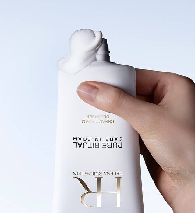 Une main presse un flacon de Pure Ritual Care-in-Foam d Helena Rubinstein, d ou ecoule une quantite de produit.
