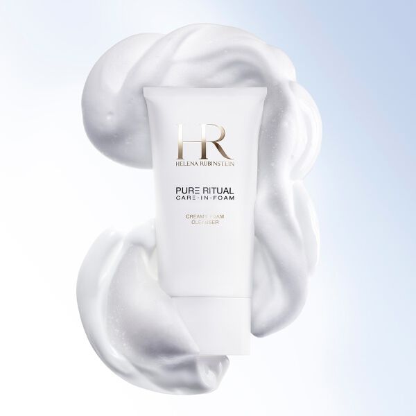 Gros plan sur le nettoyant Pure Ritual Care-in-Foam Helena Rubinstein entoure d'une mousse blanche onctueuse, a cote du visage d'une femme au teint pur et lumineux.​