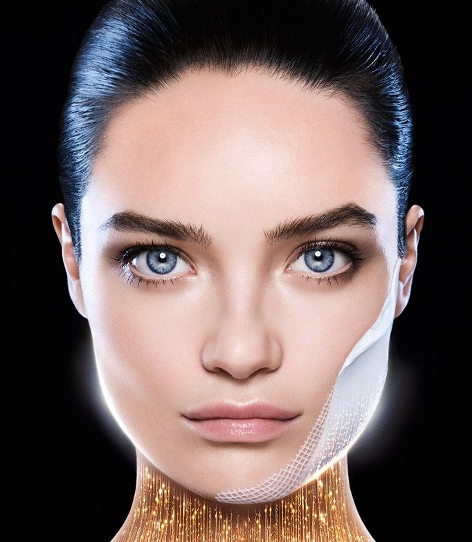 Visage de femme aux yeux bleus, avec un patch fin sur la joue. Sous son menton, un eclat dore symbolise un effet tenseur ou revitalisant. Fond noir.