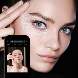 Femme aux yeux bleus appliquant un soin sous les yeux, avec une application ouverte montrant des conseils de beaute.